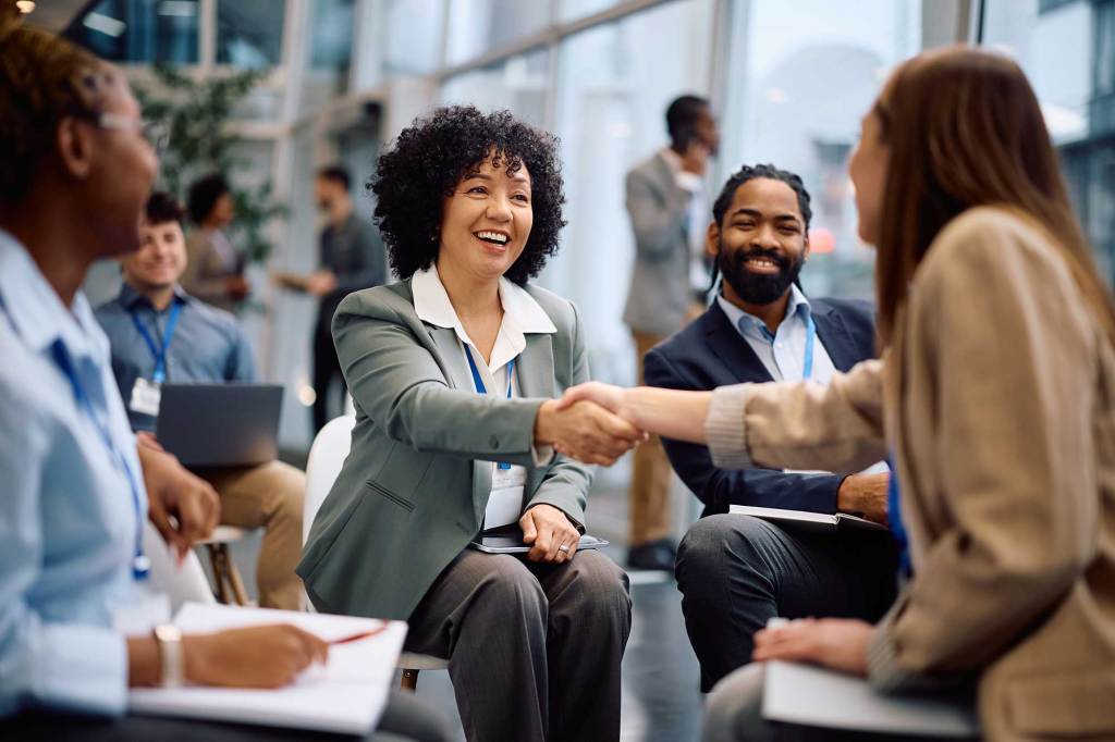 Selection Solutions Diverse professionals at a networking event, smiling as two women shake hands in a modern office setting.
